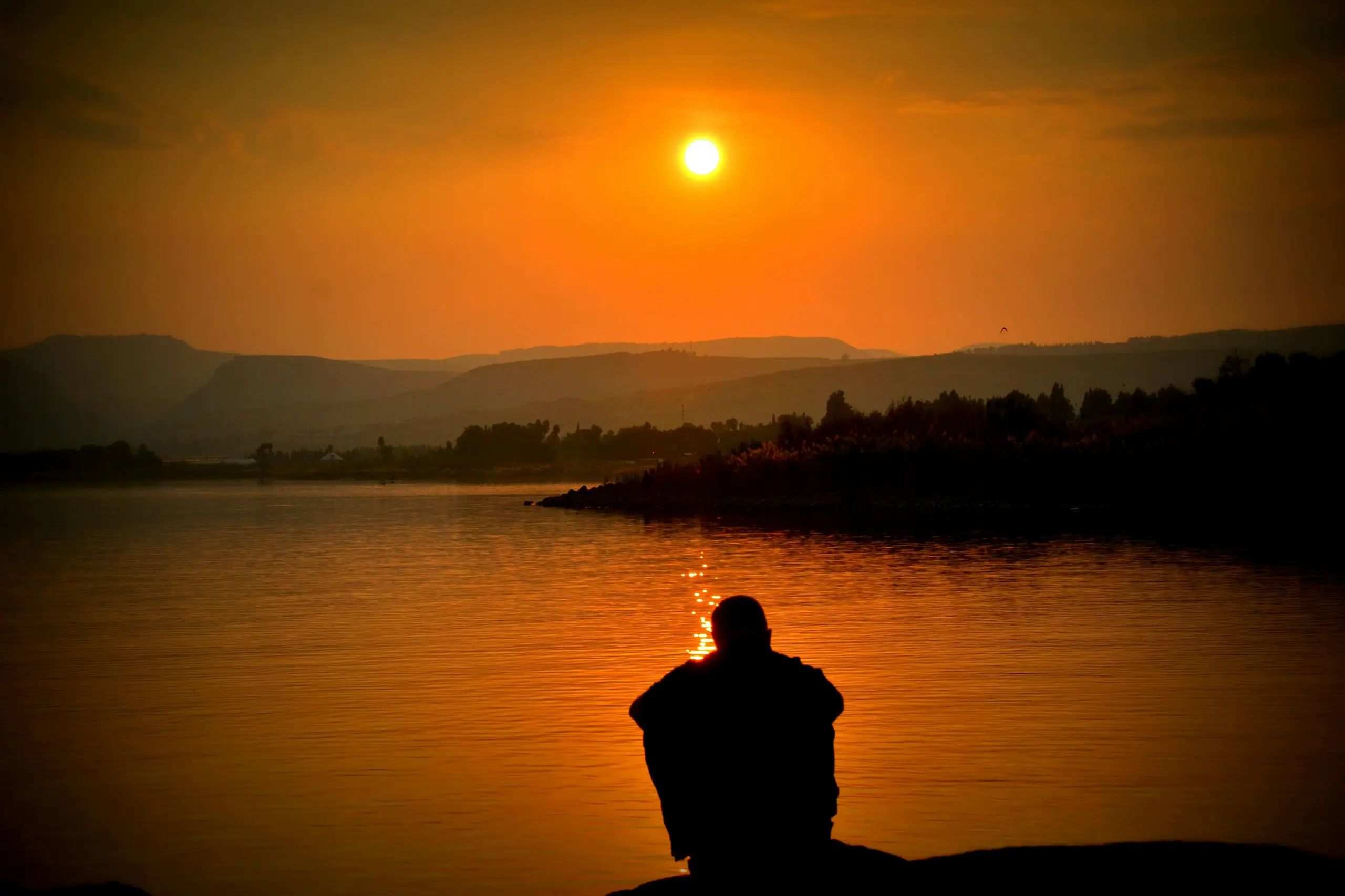 Mann sitzt vor See und schaut in Sonnenuntergang