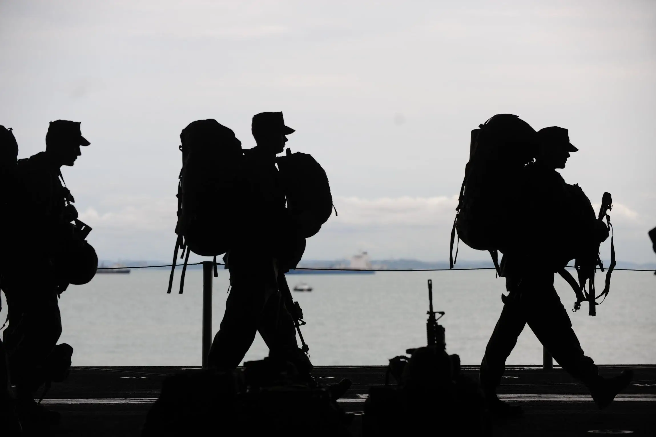Die Silhouette von drei Soldaten, die viel Gepäck und auch Waffen tragen